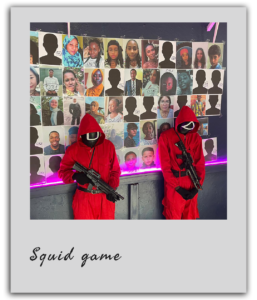 Deux participants déguisés en gardes rouges de Squid Game posent devant un mur de portraits pendant un team building à Dakar.