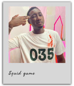 Un participant portant le numéro 035 mime une élimination humoristique avec une tache rouge sur son t-shirt pendant un team building à Dakar.