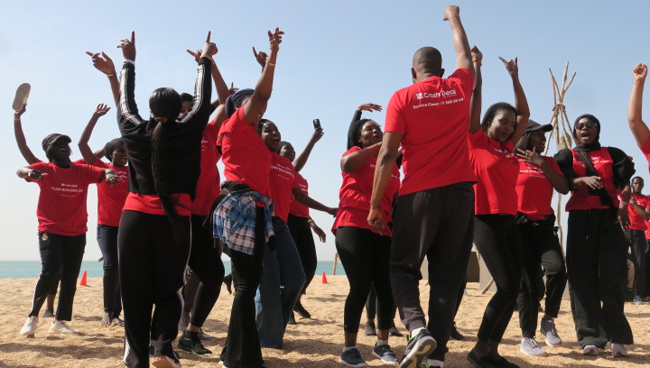 Groupe d’employés en tenue rouge participant à une activité de team building au Sénégal sur la plage.